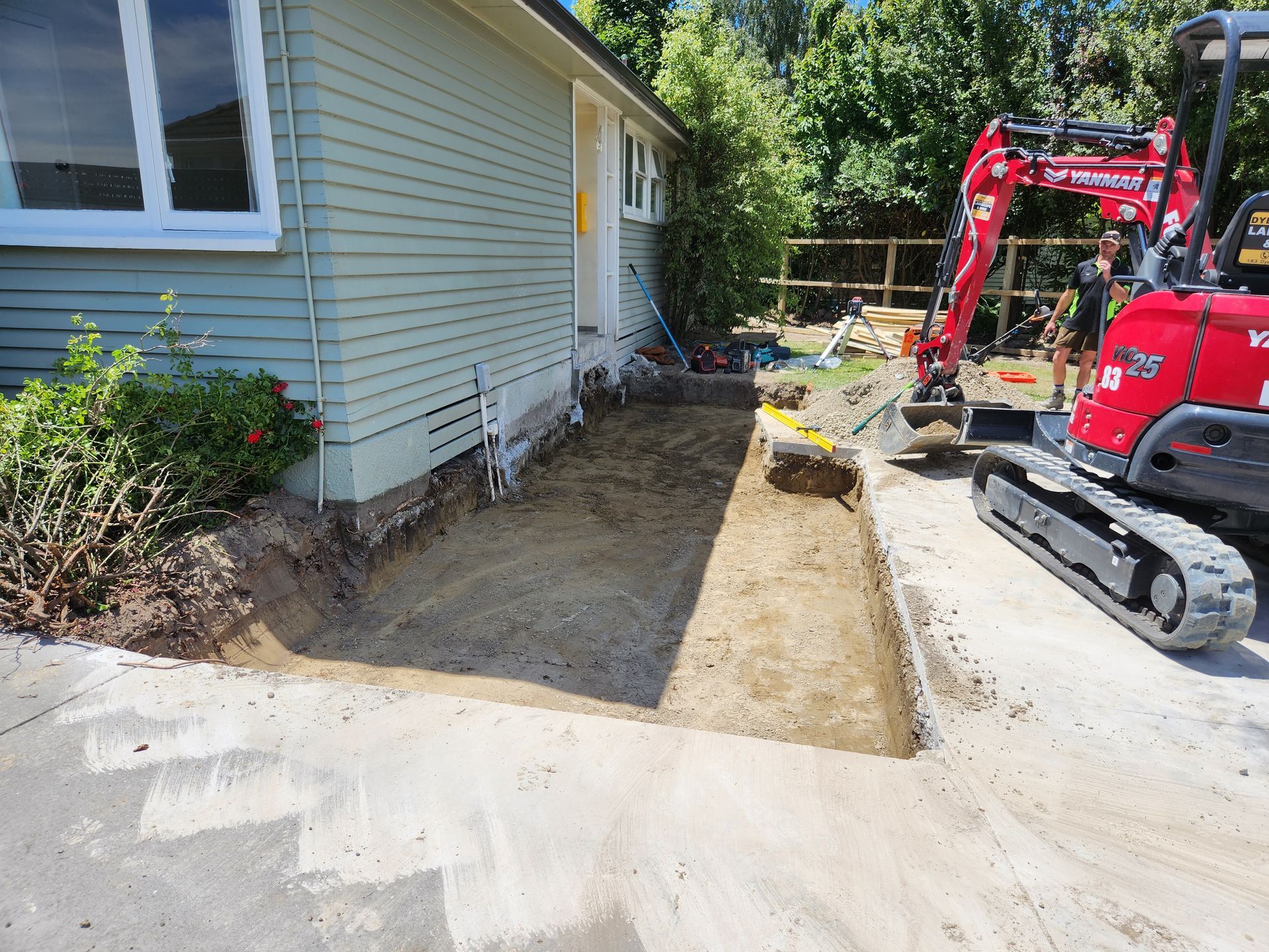 A red excavator is digging a hole in front of a house.