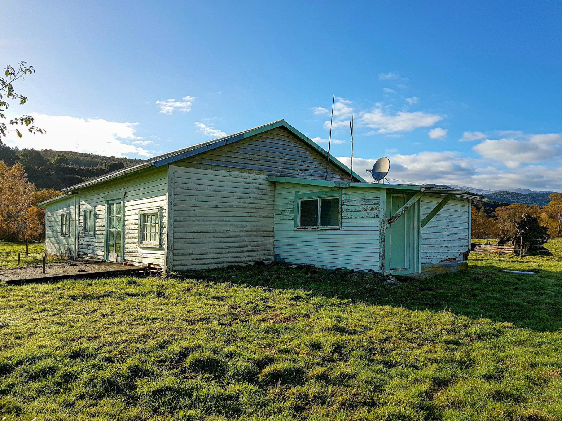 A small white house is sitting in the middle of a grassy field.