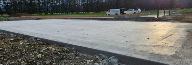 A concrete driveway is being built in a field with trees in the background.