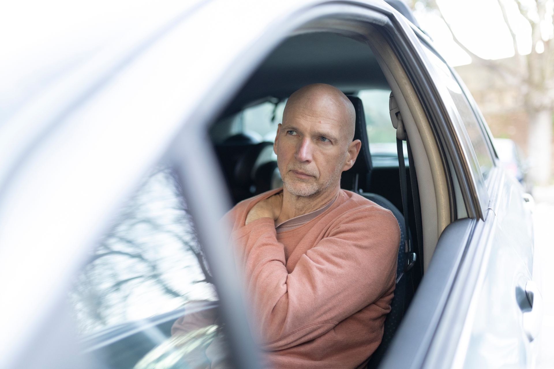Man sitting in the driver’s seat of a white car, looking out the window with a serious expression.