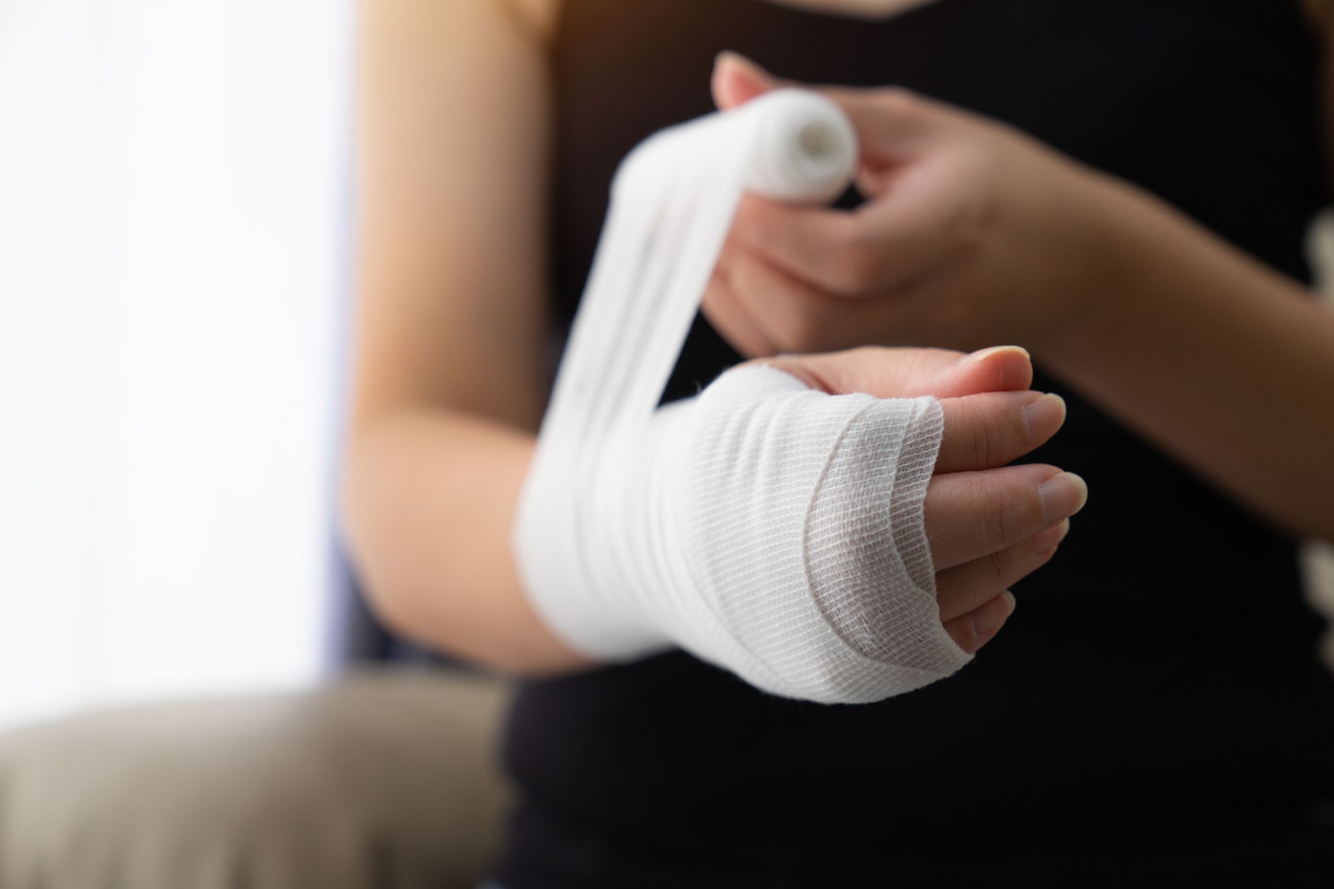 A woman is wrapping her hand in a bandage.