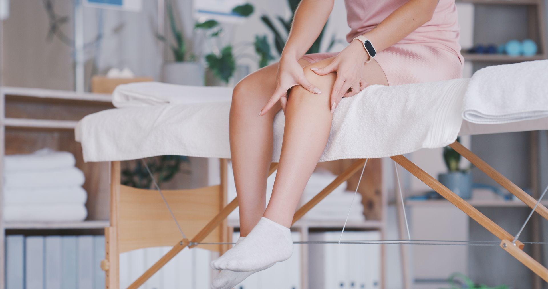 A woman is sitting on a massage table touching her leg.