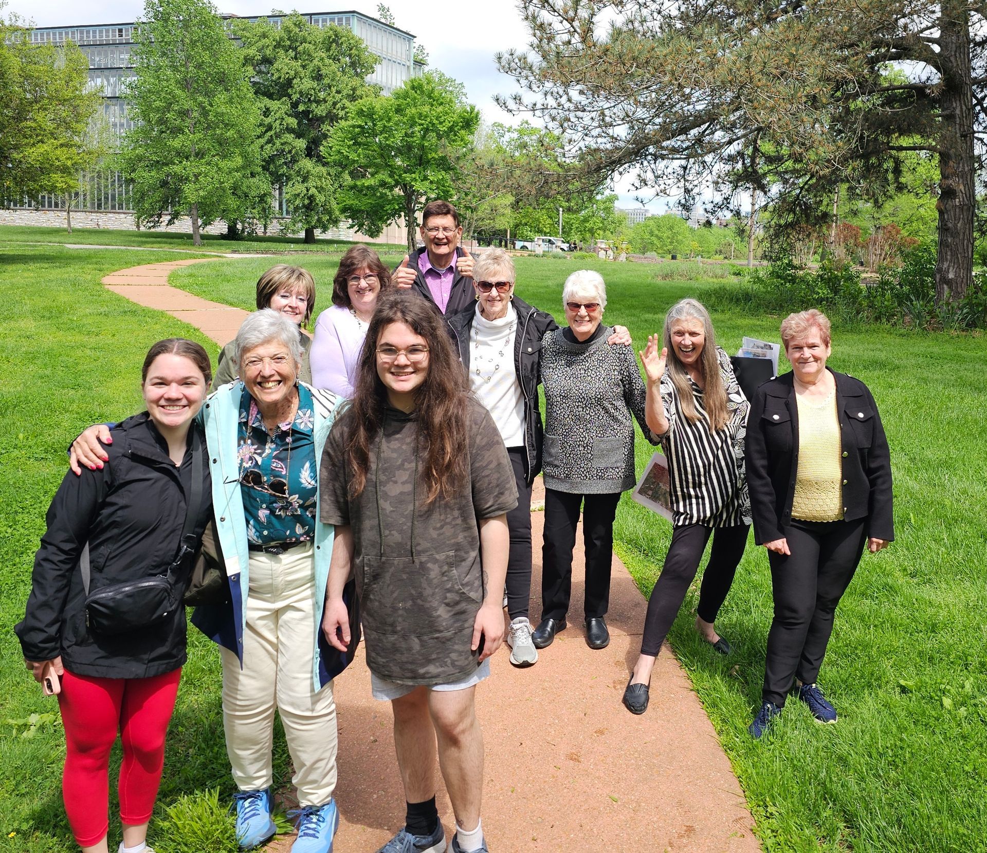 Group of people walking on a park path with green grass and trees in the background