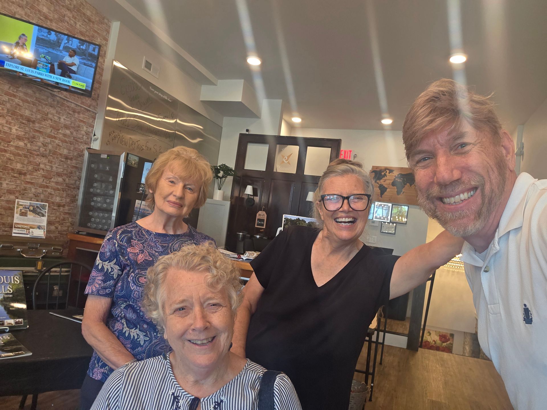 Four smiling people posing in a restaurant interior, with brick walls and warm ceiling lights.