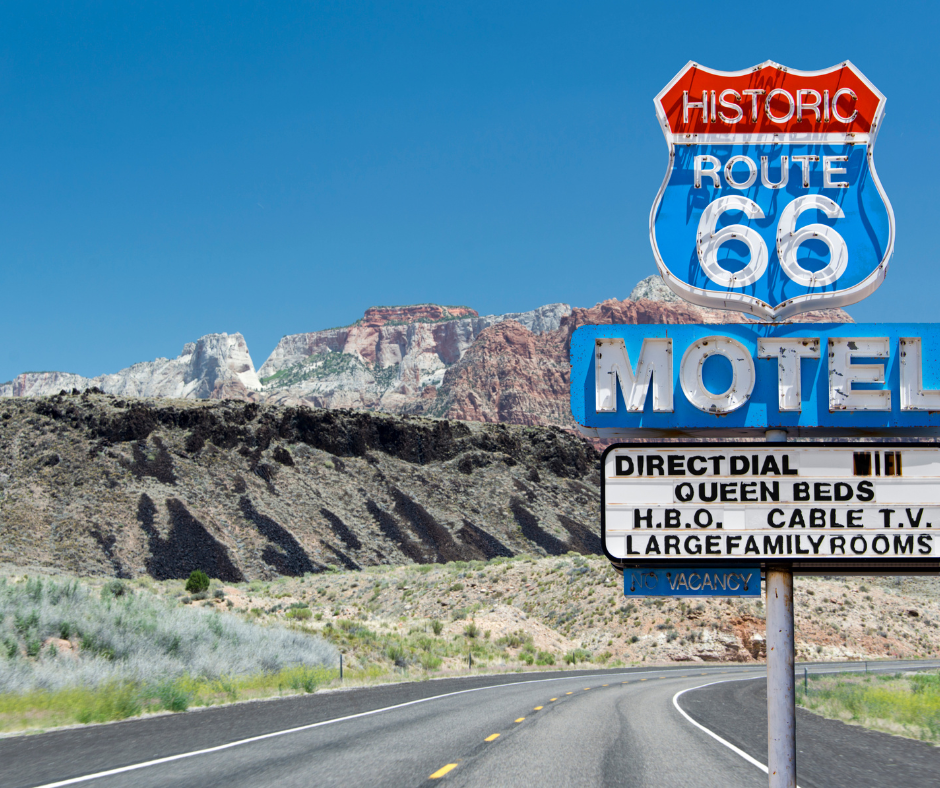 Route 66 motel sign with a desert mountain backdrop and blue sky.