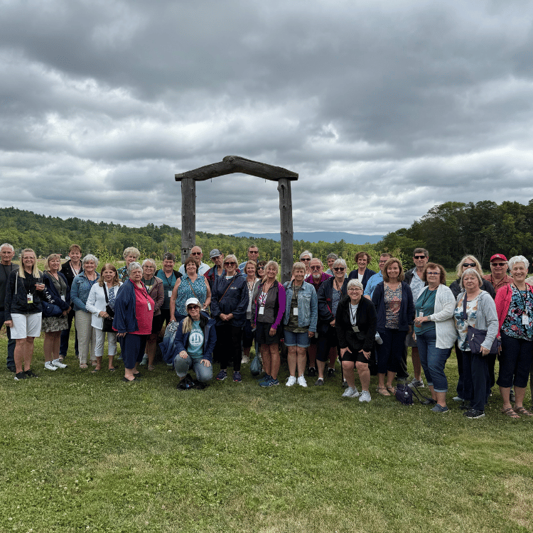 Group of people posing outdoors with a wooden arch in the background under a cloudy sky.