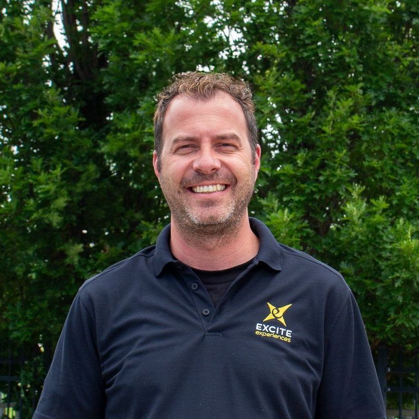 Man in black polo shirt smiling outdoors; 