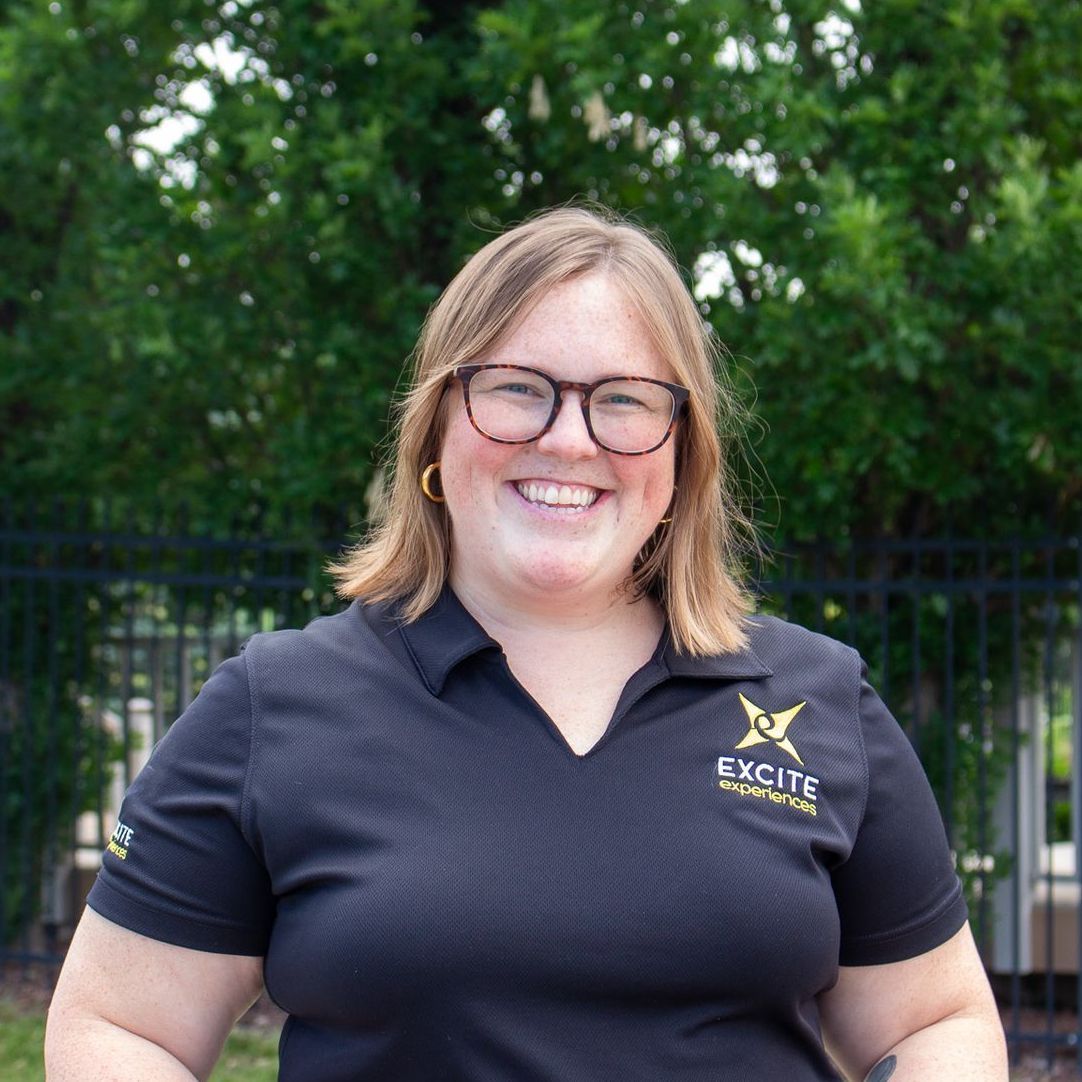 Woman with glasses smiles; wearing black polo shirt with 