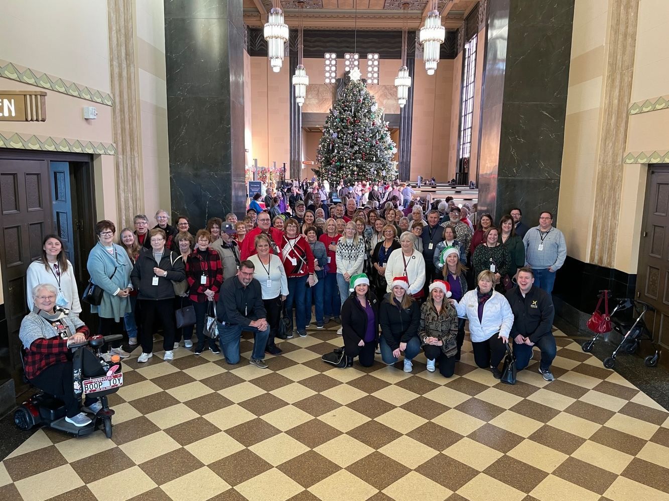 A large group of people are posing for a picture in front of a christmas tree.