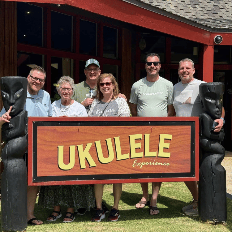 Group poses with Ukulele Experience sign outside building.