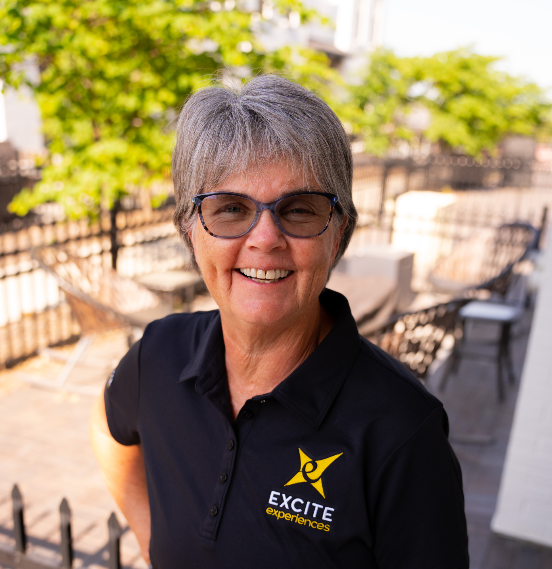Woman in black shirt with glasses smiles outdoors with 