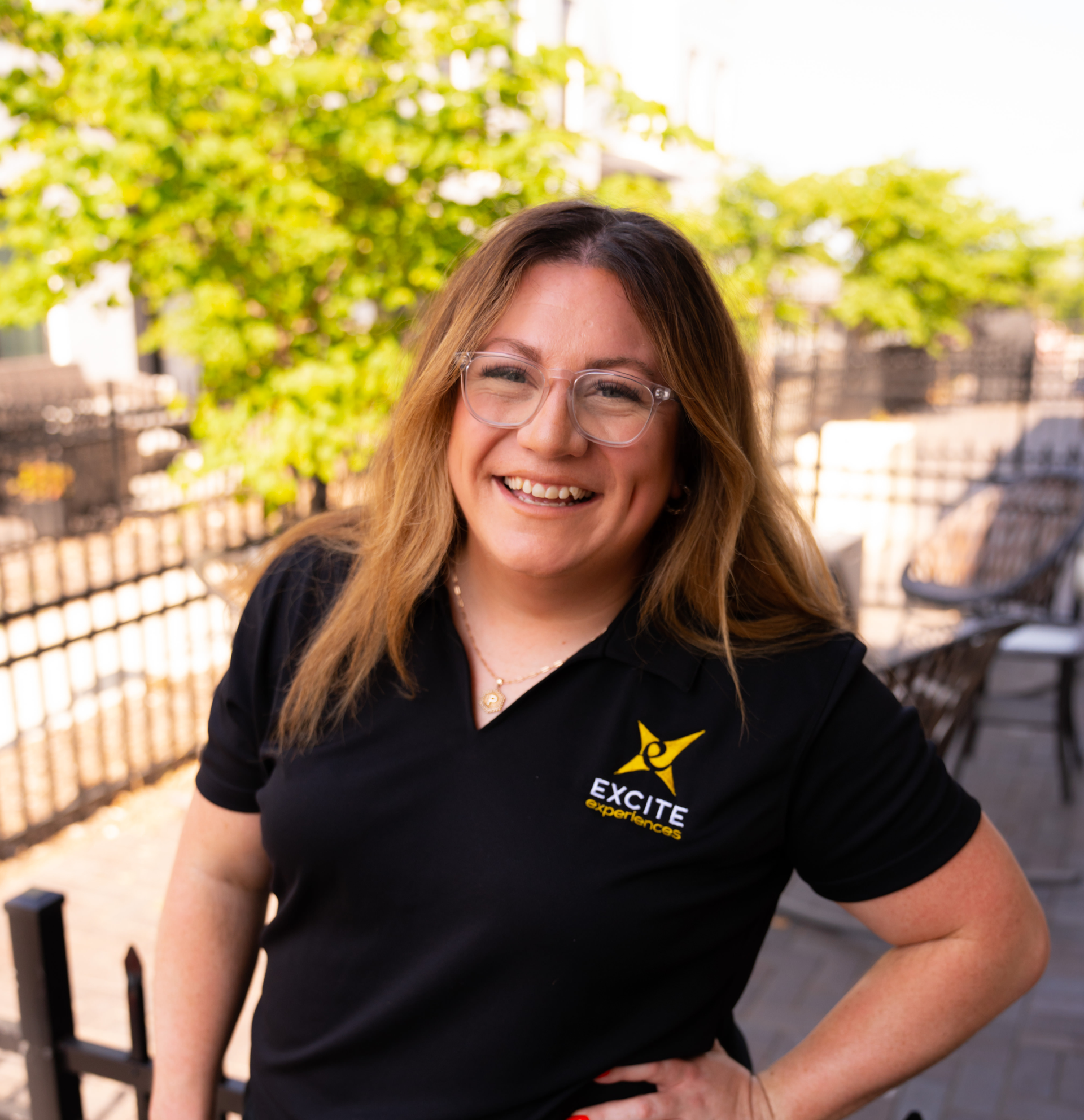 Woman in black polo shirt smiling outdoors, hand on hip. 