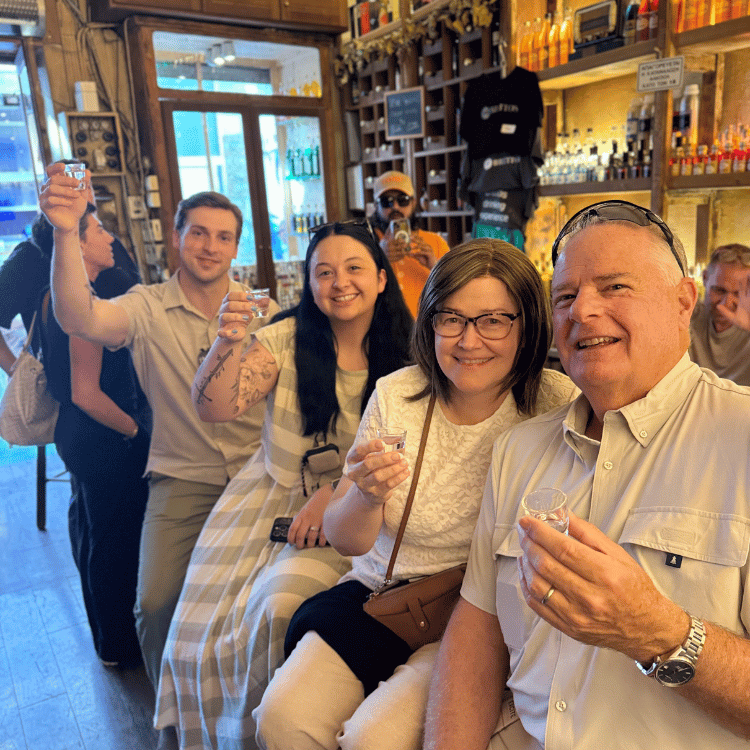 Group of people toasting with clear shots in a bar. Smiling, casual attire, wooden interior.