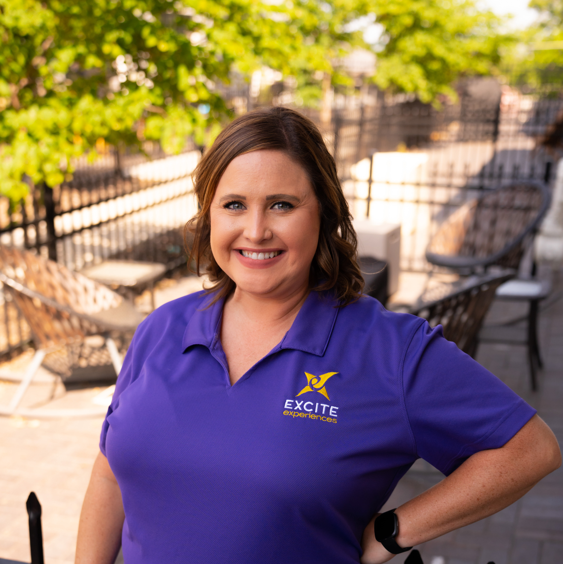 Woman in purple shirt, smiling, outdoors; logo says 