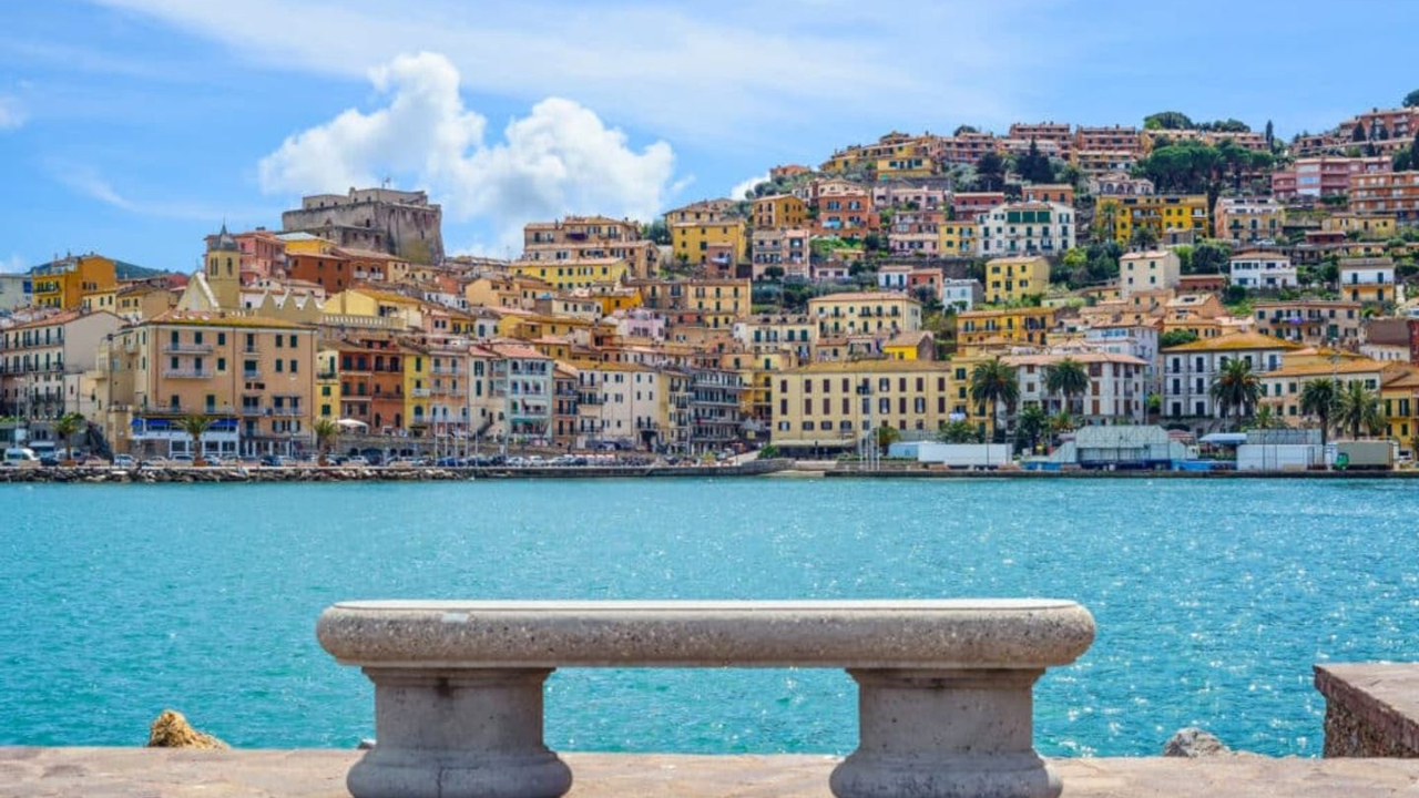 A bench in front of a body of water with a city in the background.