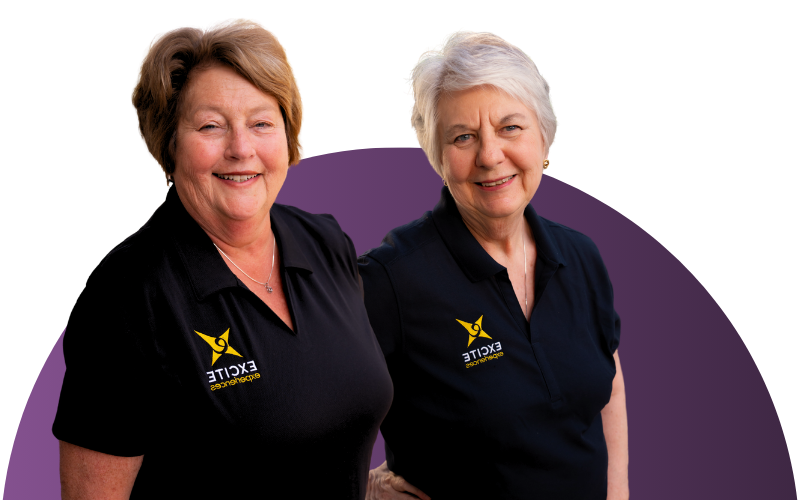 Two women in black polo shirts smile, set against a purple backdrop.