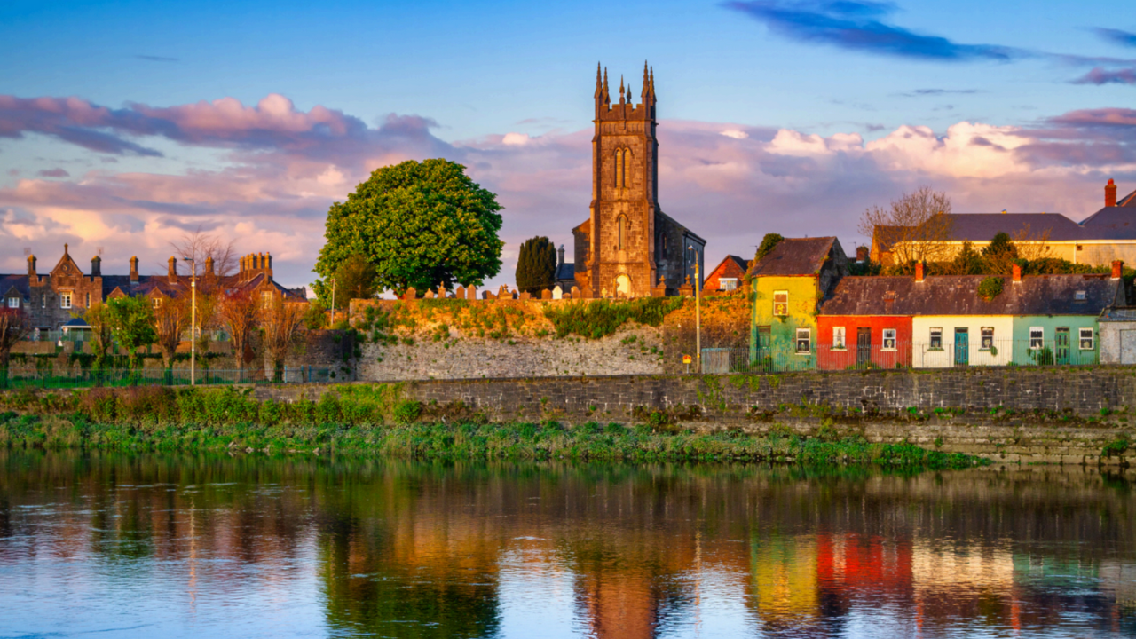 A church is sitting on top of a hill next to a body of water.