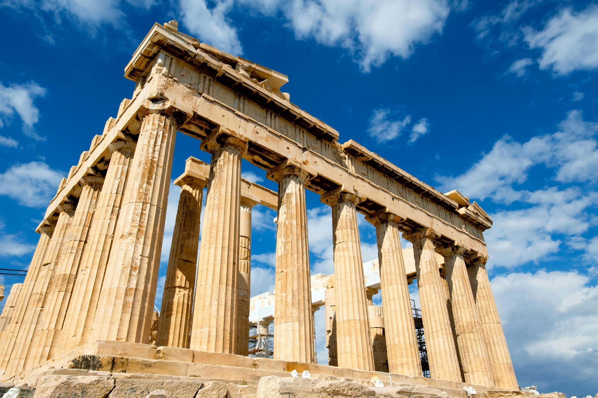 Parthenon ruins with Doric columns against a bright blue sky with clouds.