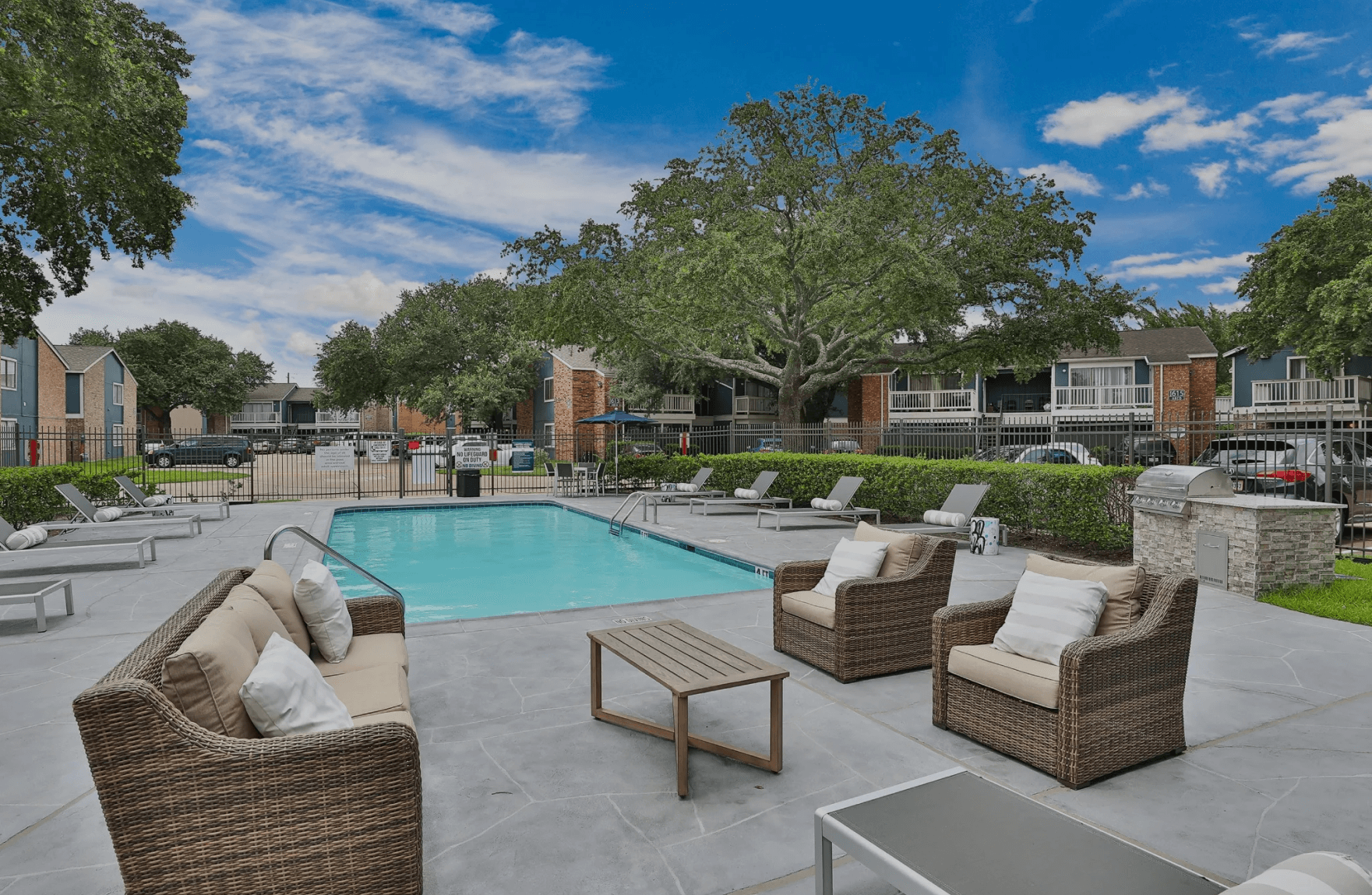 A swimming pool with a couch , chairs and a table in front of it.