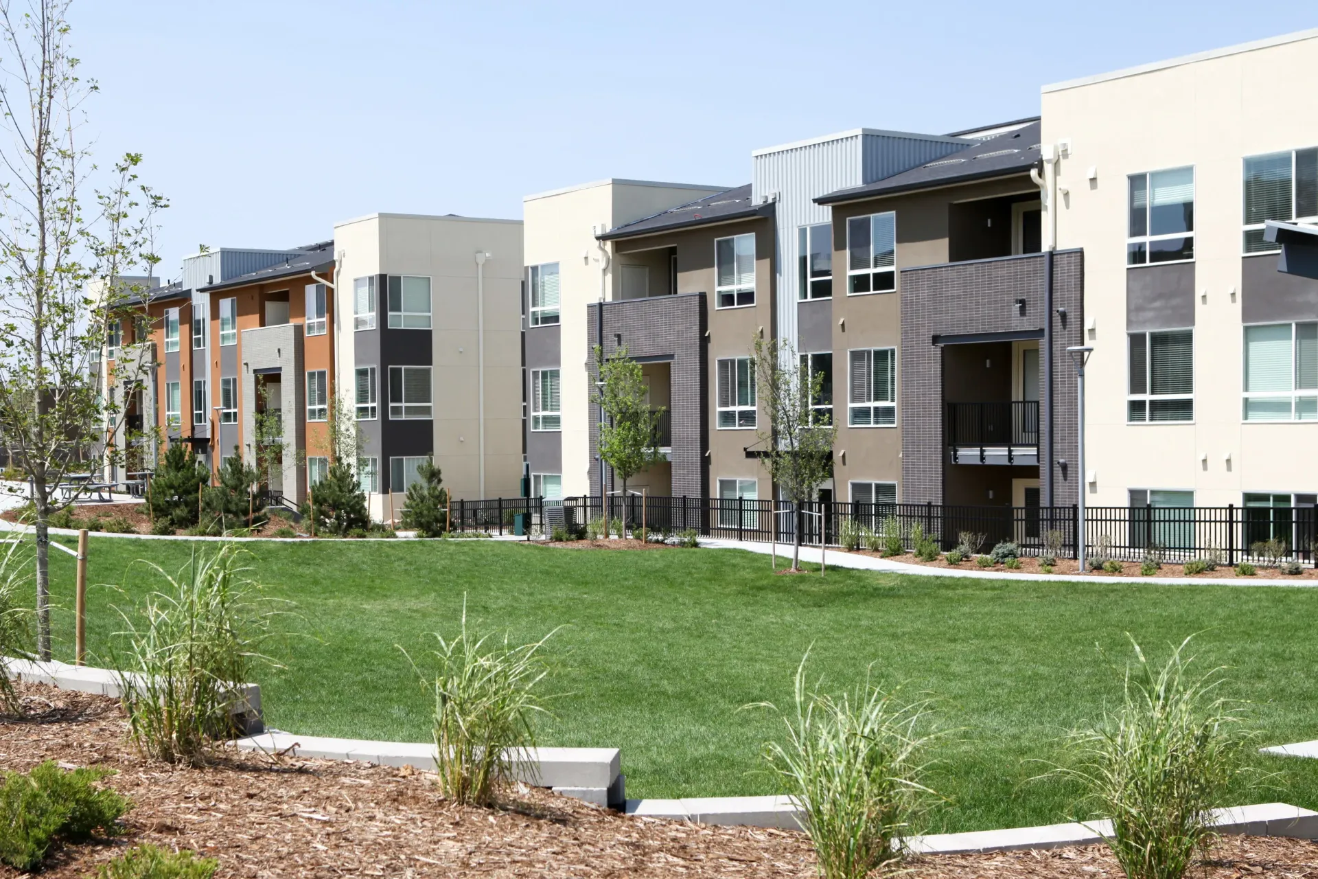 A row of apartment buildings with a lush green lawn in front of them.