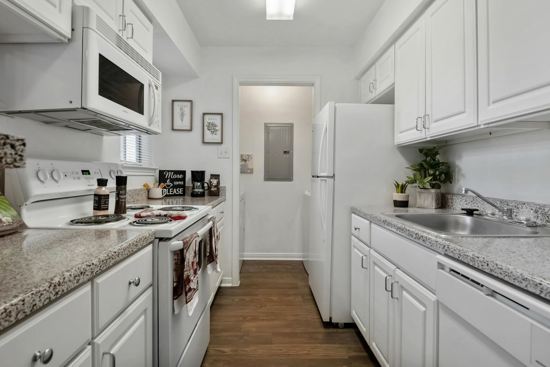 Compact white kitchen in an apartment with stove, microwave, refrigerator, and granite countertops.