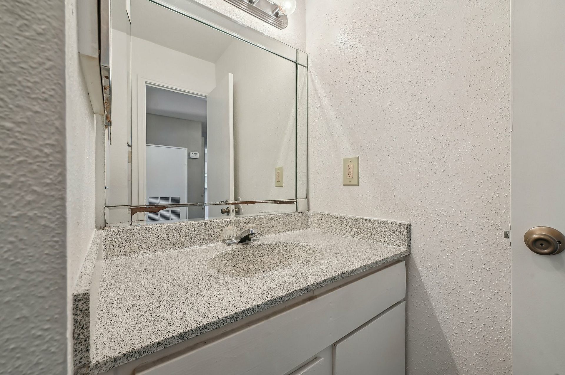 Bathroom vanity with speckled countertop, sink, and mirrored medicine cabinet.