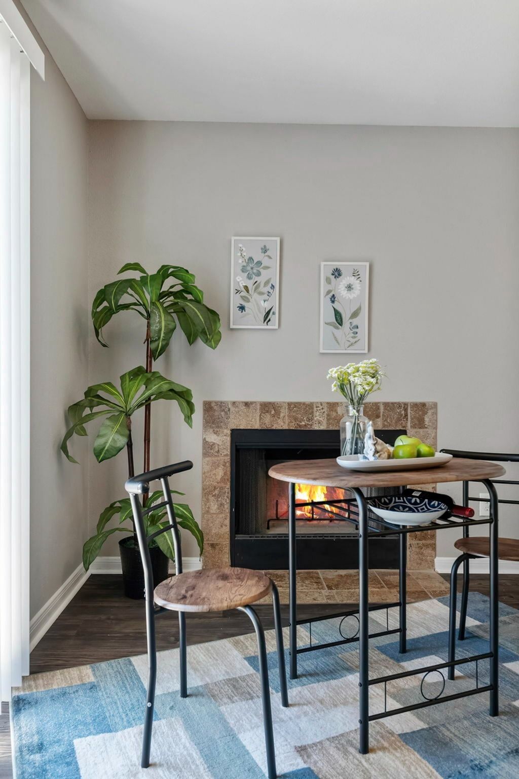 Interior living area with a fireplace, round wood table, metal chairs, and a potted plant.