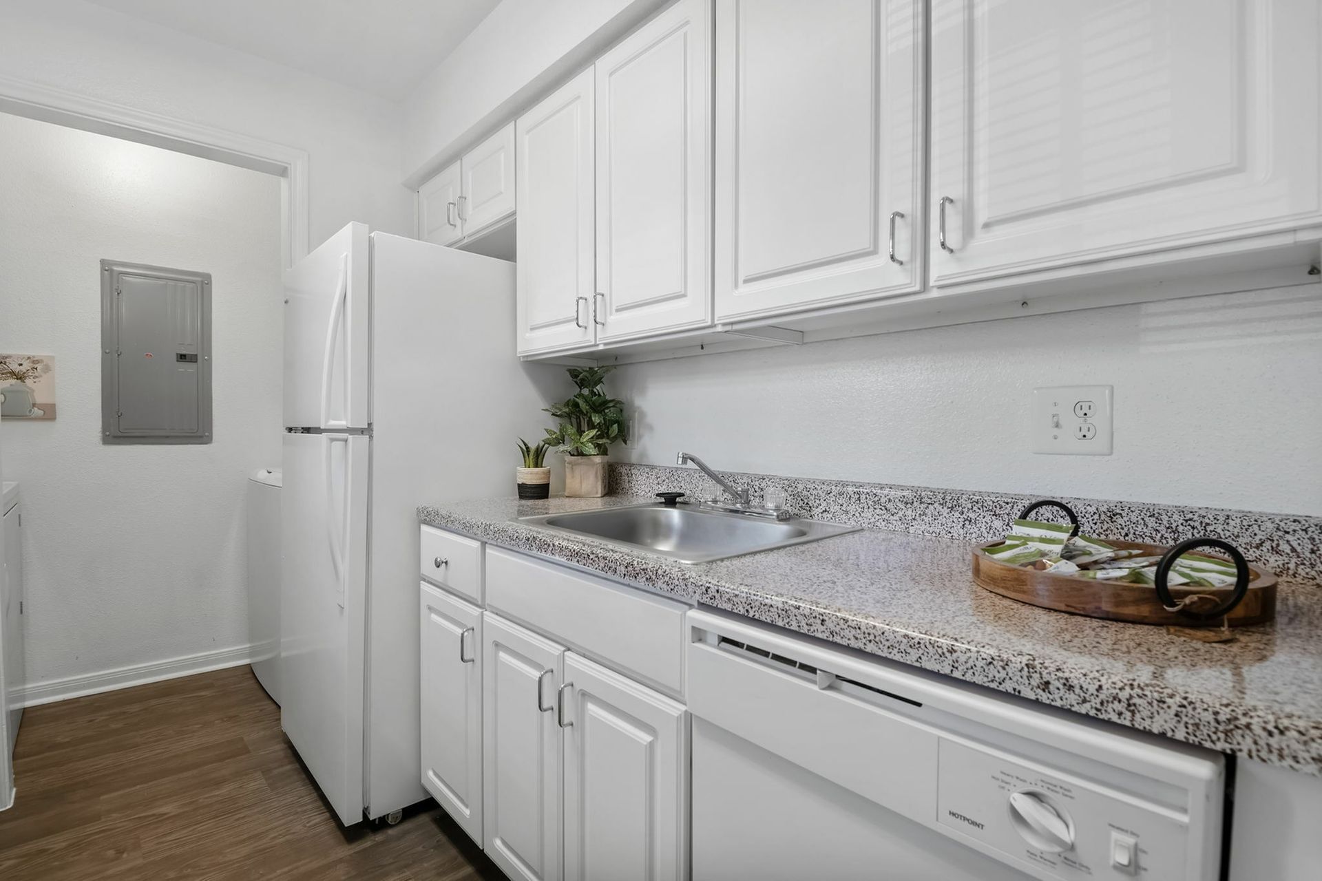 White kitchen with granite countertops, sink, white cabinets, refrigerator, and dishwasher.