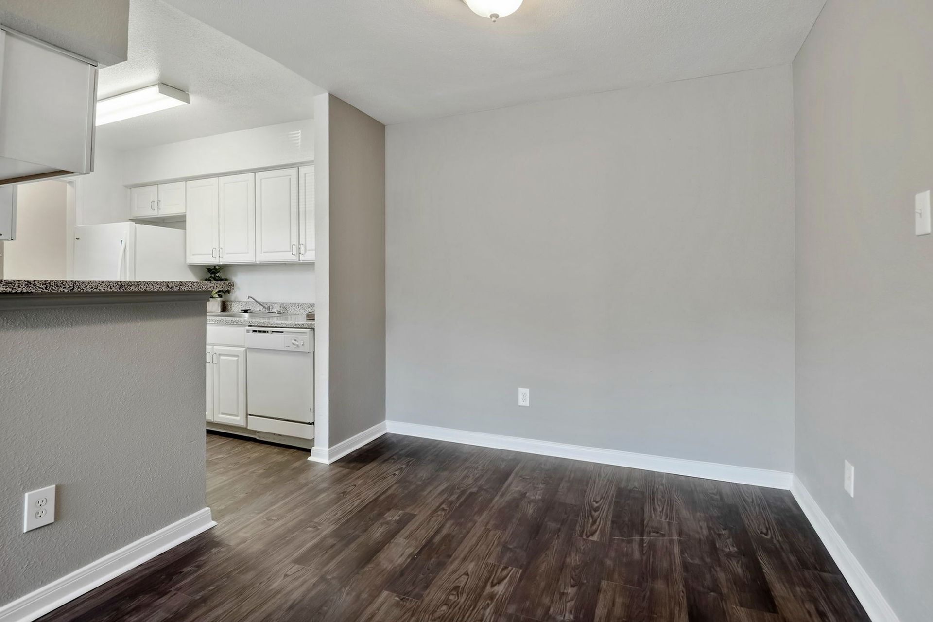 Interior view of an apartment kitchen with white cabinets, granite counters, and dark wood flooring.