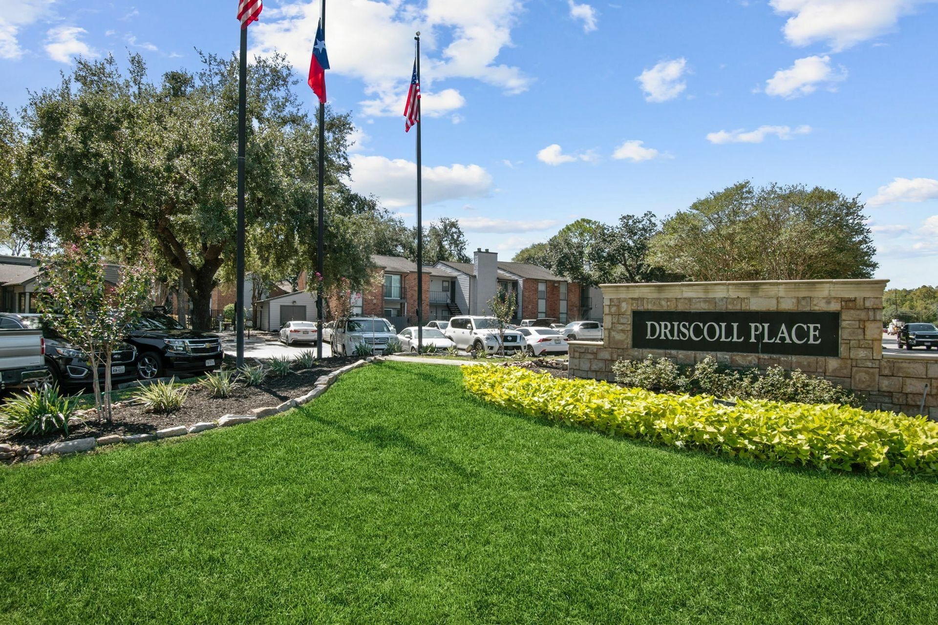 Entrance to Driscoll Place community with flags, manicured lawn, and parked cars.