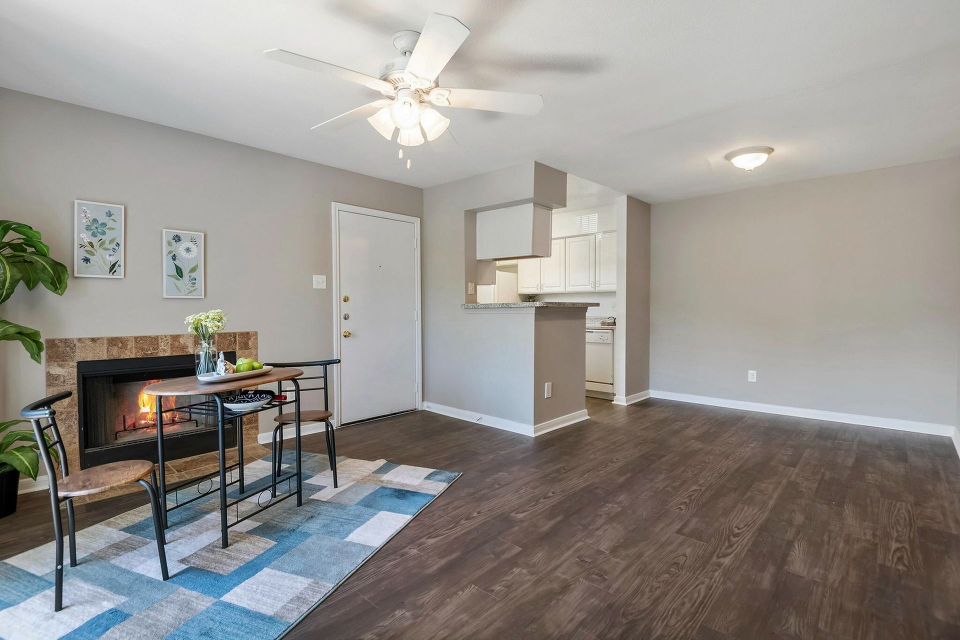 Living room with a fireplace, ceiling fan, small dining table, and open kitchen.