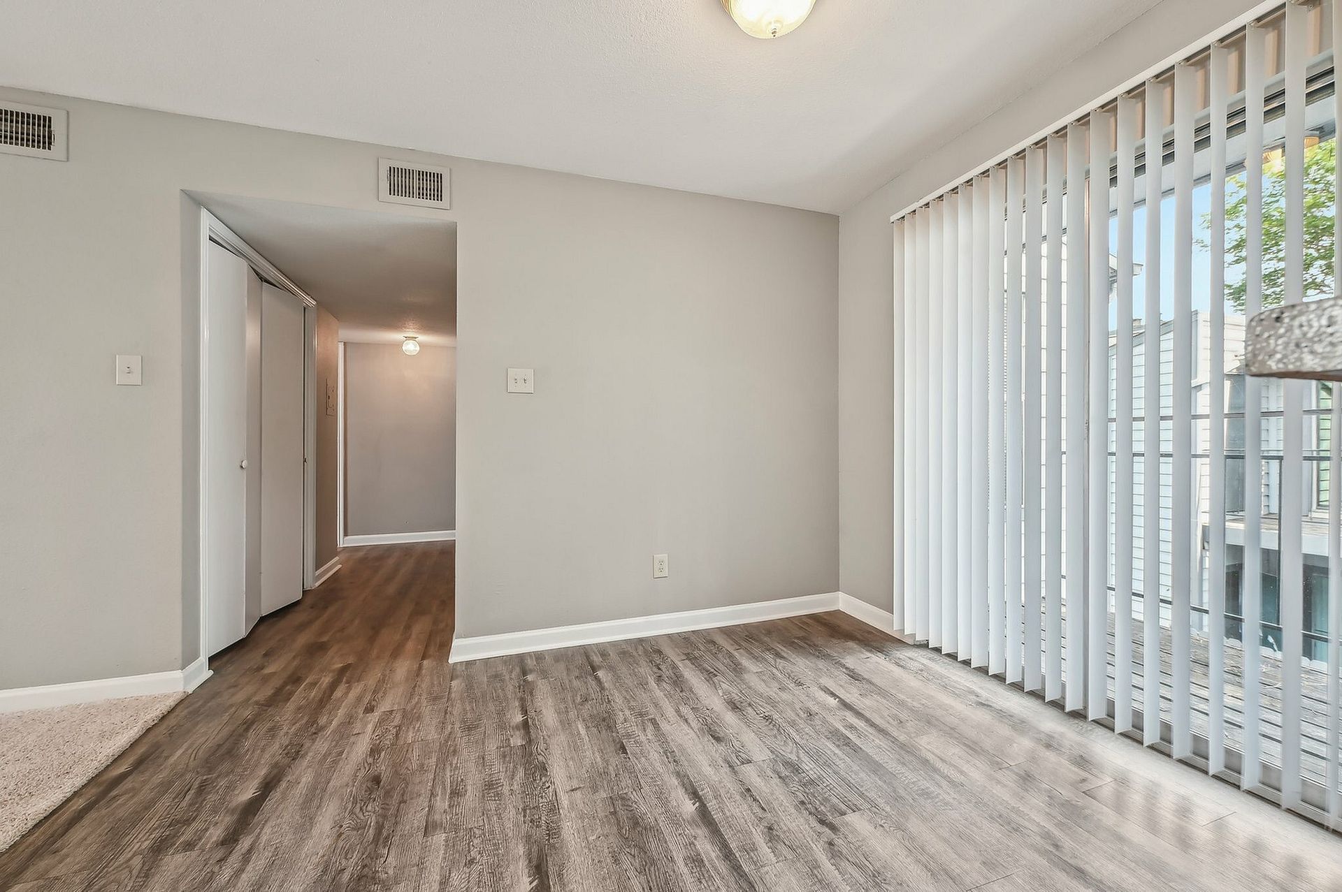 Living area with large window and vertical blinds, gray walls, and wood-look flooring.