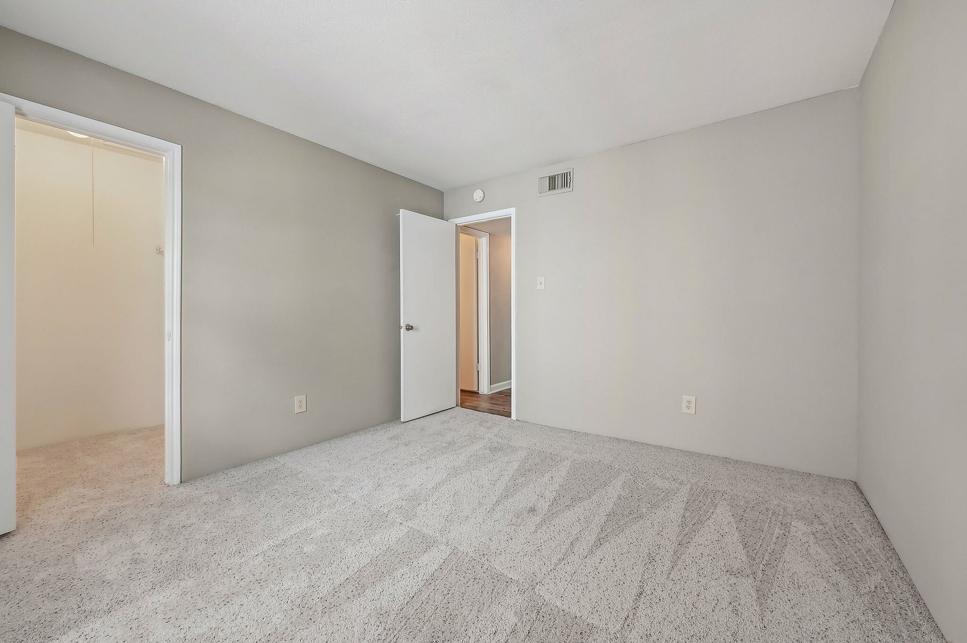 Empty bedroom with light gray walls, white trim, carpet, and a door to the hallway.