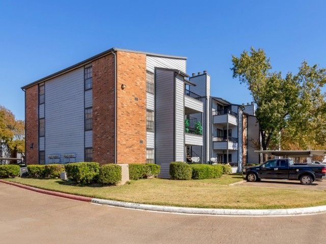 Exterior view of a multi-story apartment building with landscaping and parked cars.