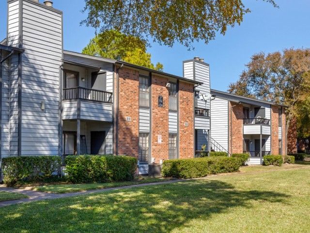 Exterior view of a two-story brick-and-siding apartment building with balconies and a grassy lawn.