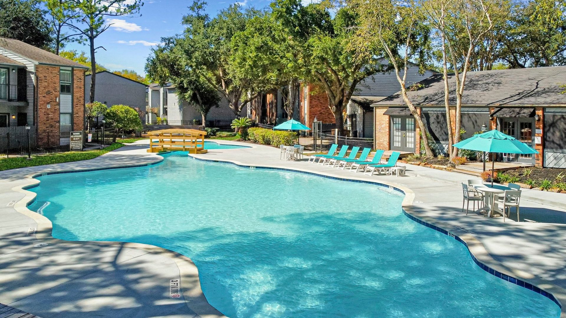 Outdoor apartment community pool with turquoise water, lounge chairs and umbrellas.