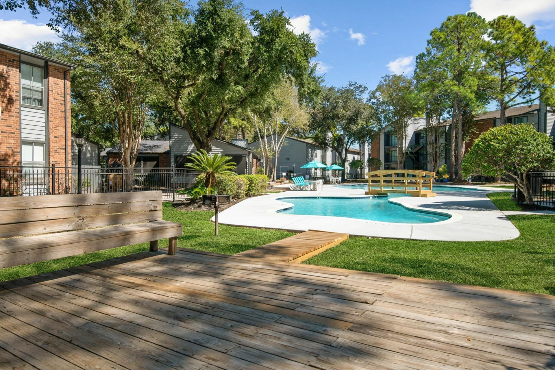 Outdoor community pool area with lounge chairs, umbrellas, and trees.