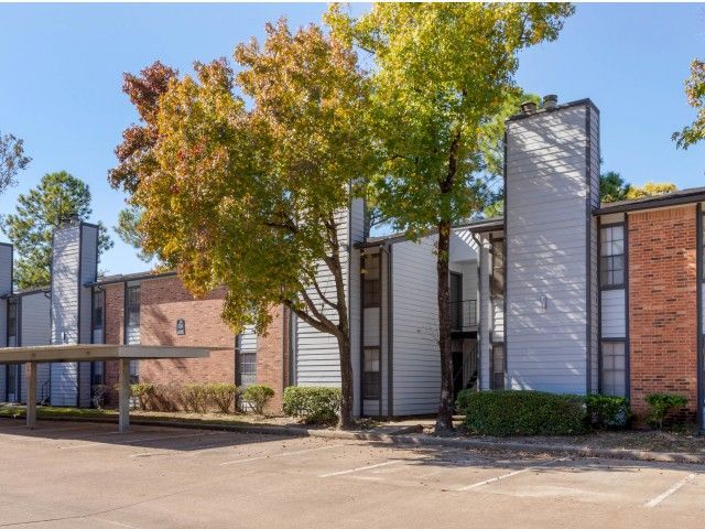 Exterior view of a multifamily building with brick and light siding, trees, and a parking lot.