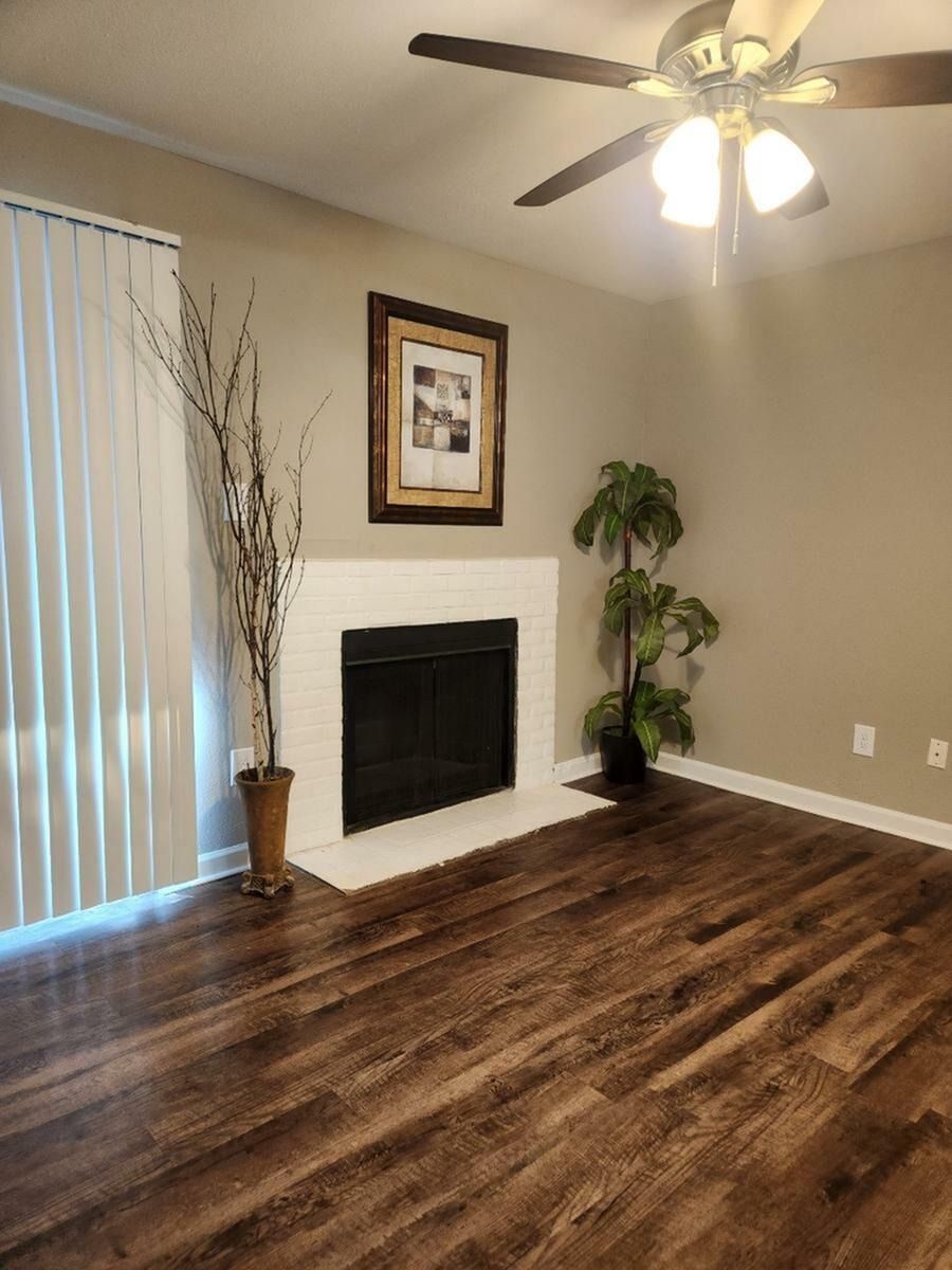 Living room with white brick fireplace, ceiling fan, and wood-style flooring.