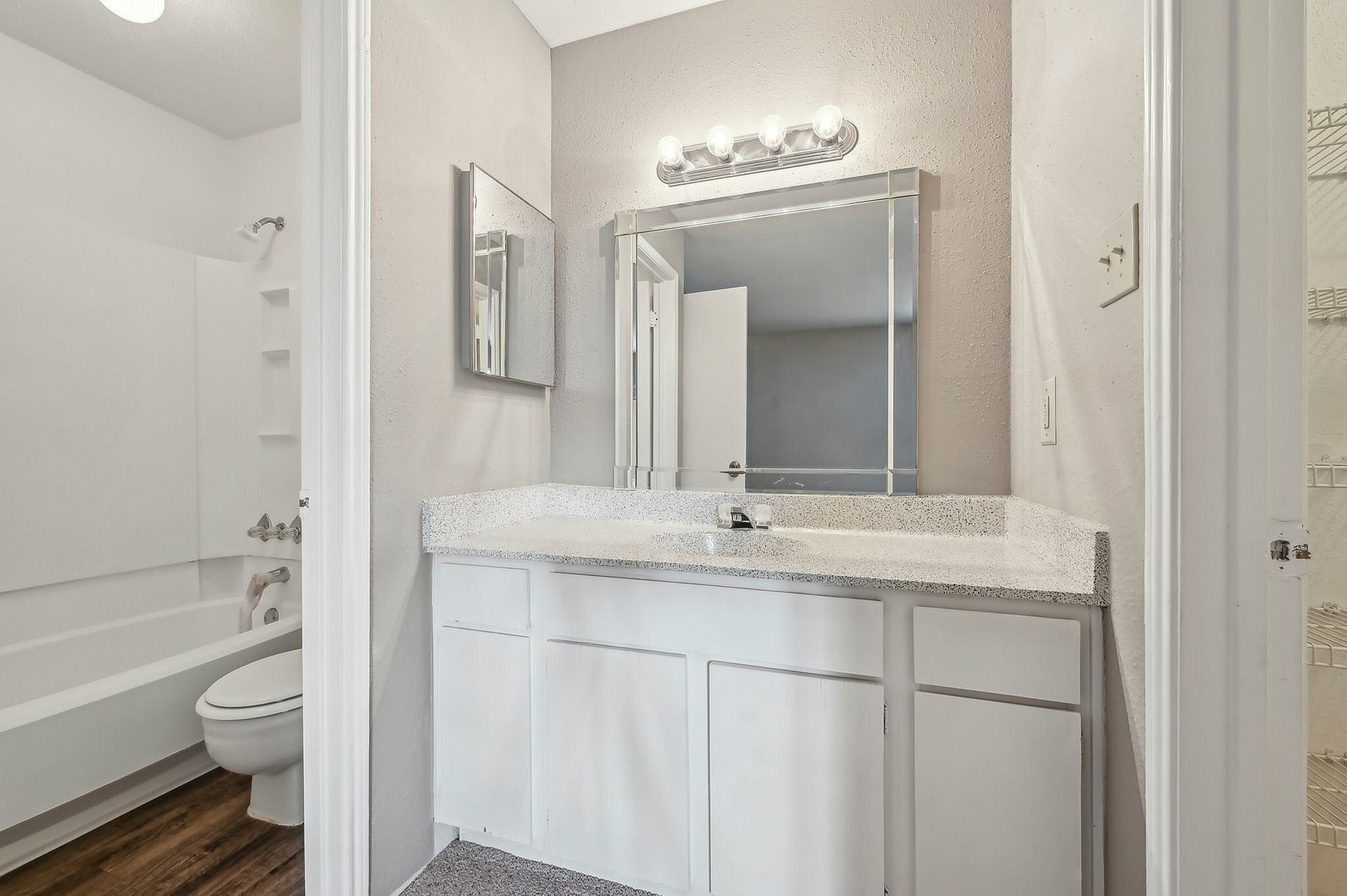 Bathroom vanity with white cabinets, speckled countertop, mirror, and light fixture.