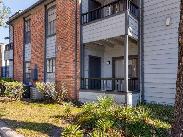 Exterior view of a two-story apartment building with brick and gray siding, small balconies, and landscaped shrubs.