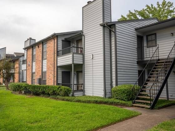 Exterior view of a modern apartment complex with balconies, stairwells, and green lawn.
