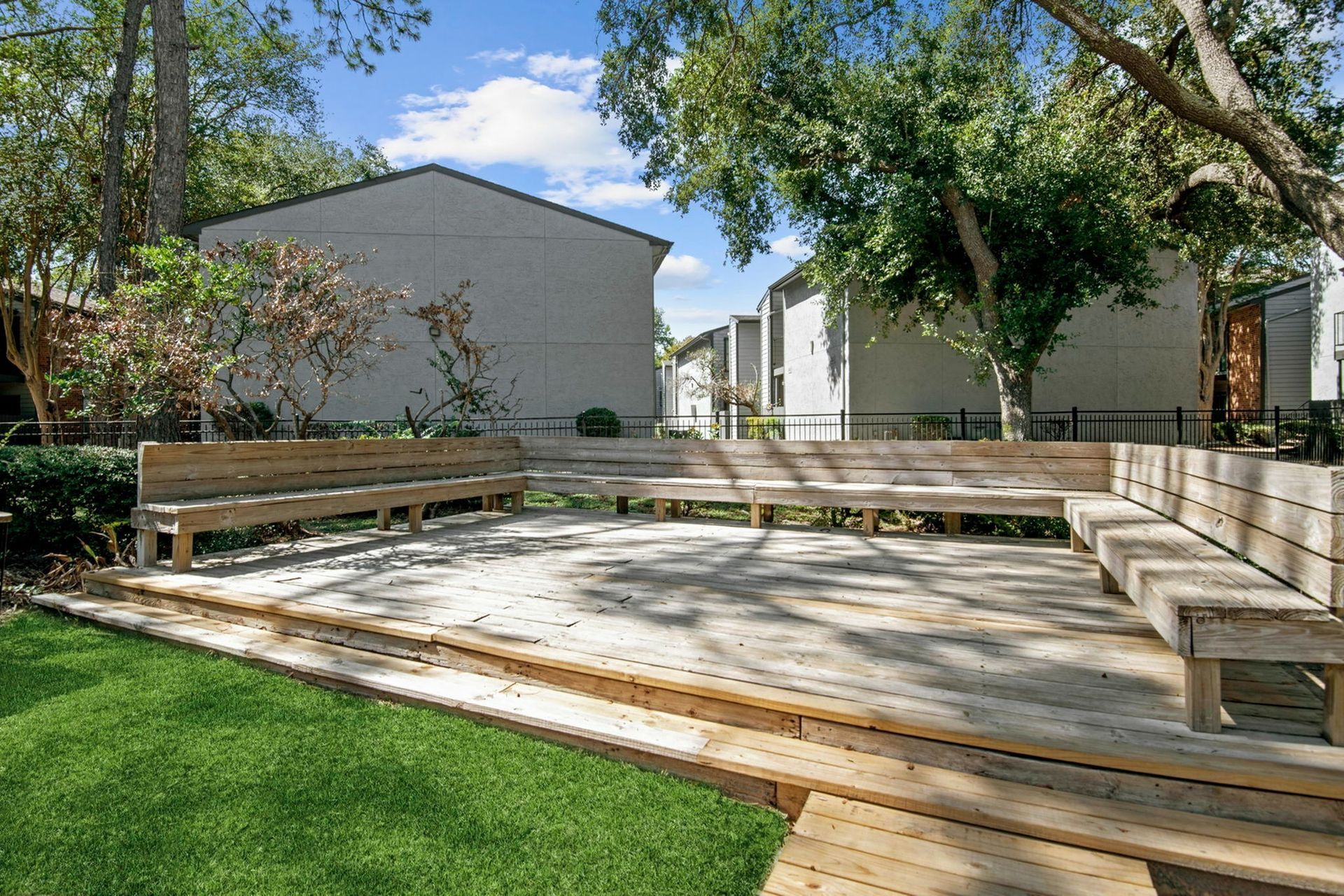 Outdoor communal wooden deck with built-in benches and trees in a courtyard.