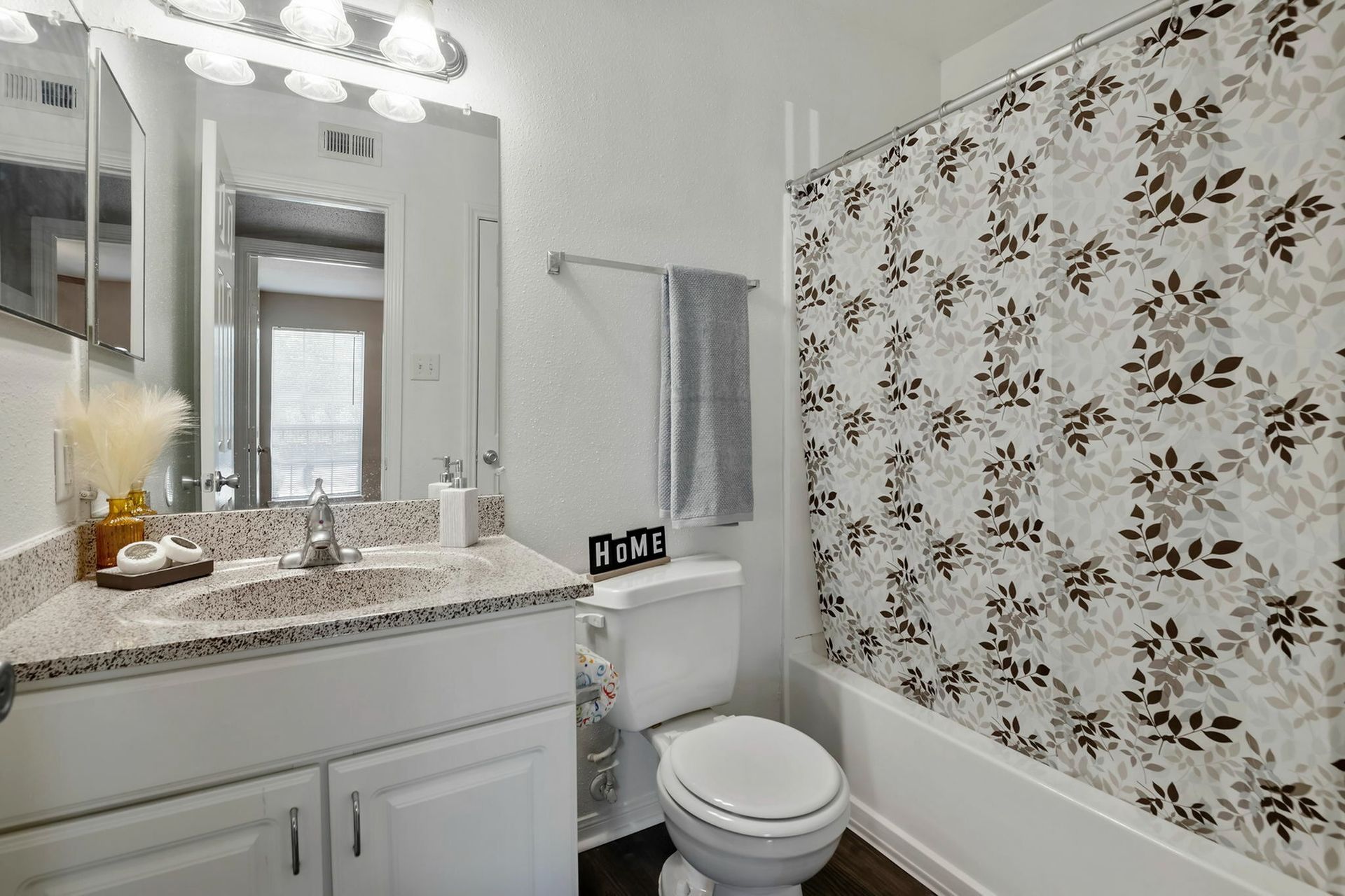Bathroom with vanity, mirror, toilet, and a beige-brown leaf-pattern shower curtain.