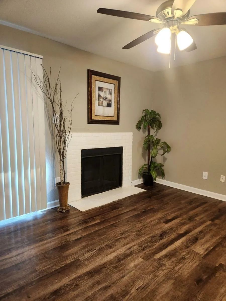 Living room with fireplace, hardwood floor, tall plant, picture frame, and ceiling fan.