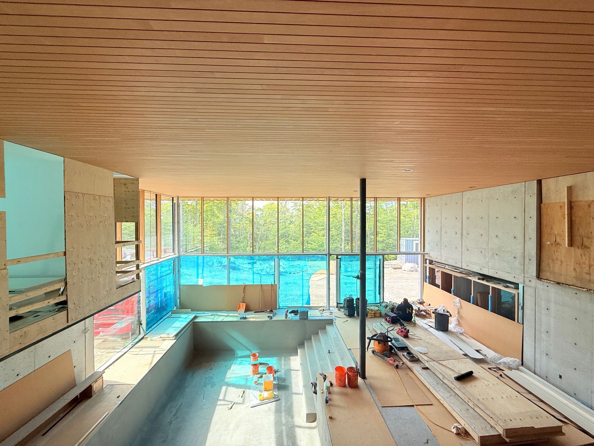 Intérieur d'un chantier de construction moderne avec piscine, baies vitrées et plafond en bois.