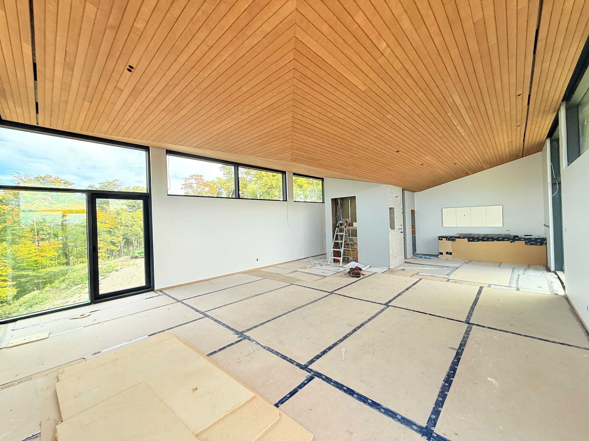 Pièce moderne vide avec plafond en bois incliné, grandes fenêtres et sol délimité par du ruban adhésif