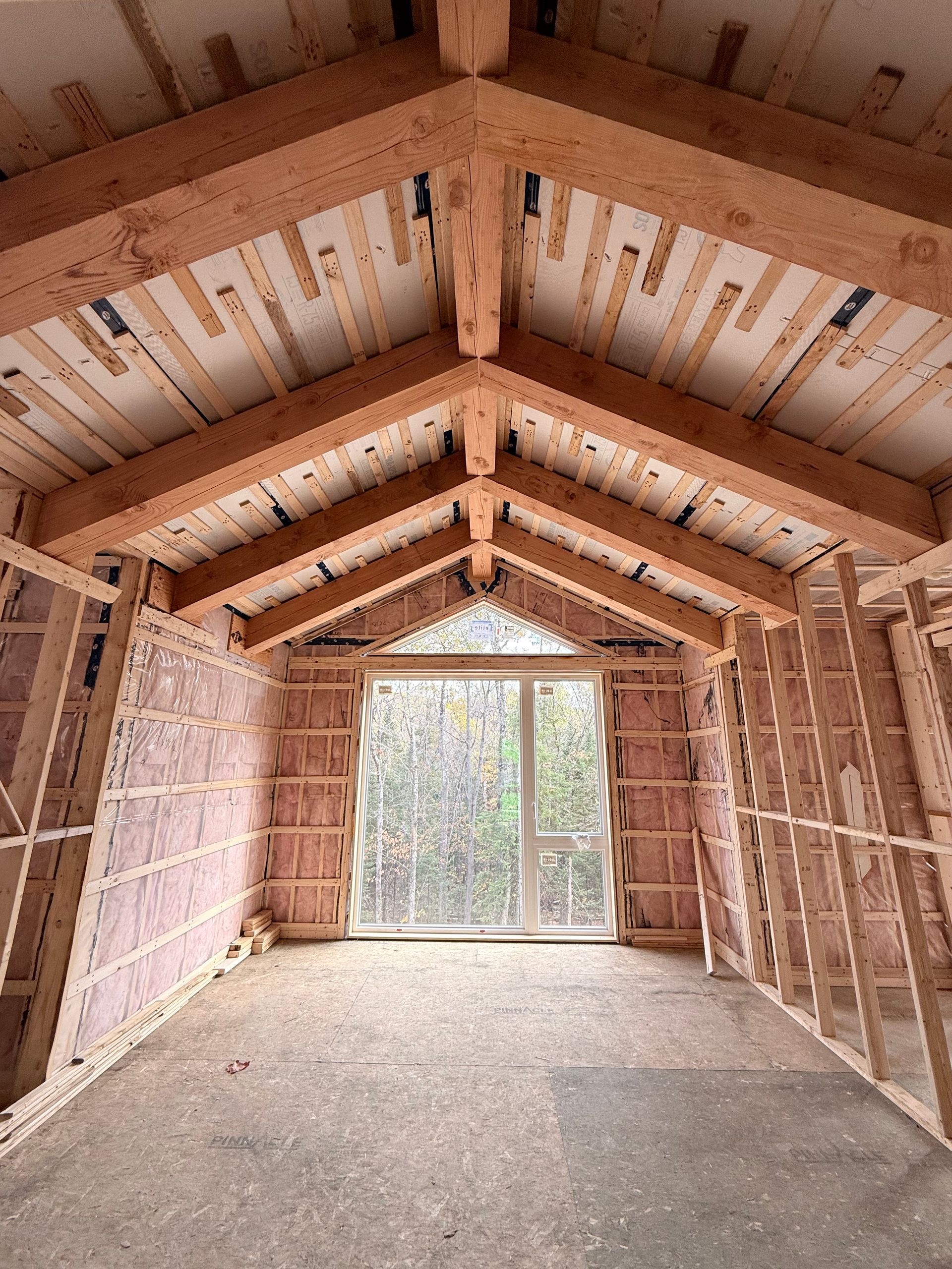 Intérieur d'une structure à ossature bois, non finie avec isolation et une grande fenêtre, tons de bois clair.