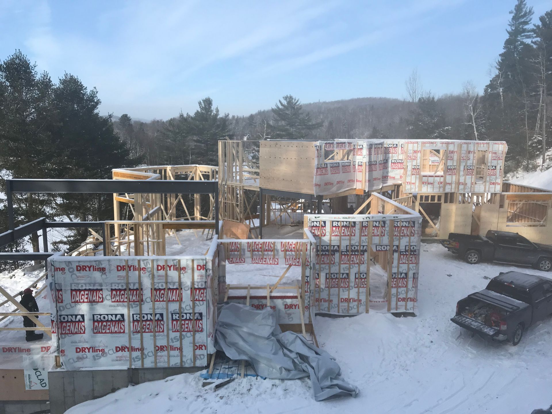 Chantier de construction, charpente de maison sous la neige. Montants en bois, revêtement avec pare-vapeur, voitures stationnées.