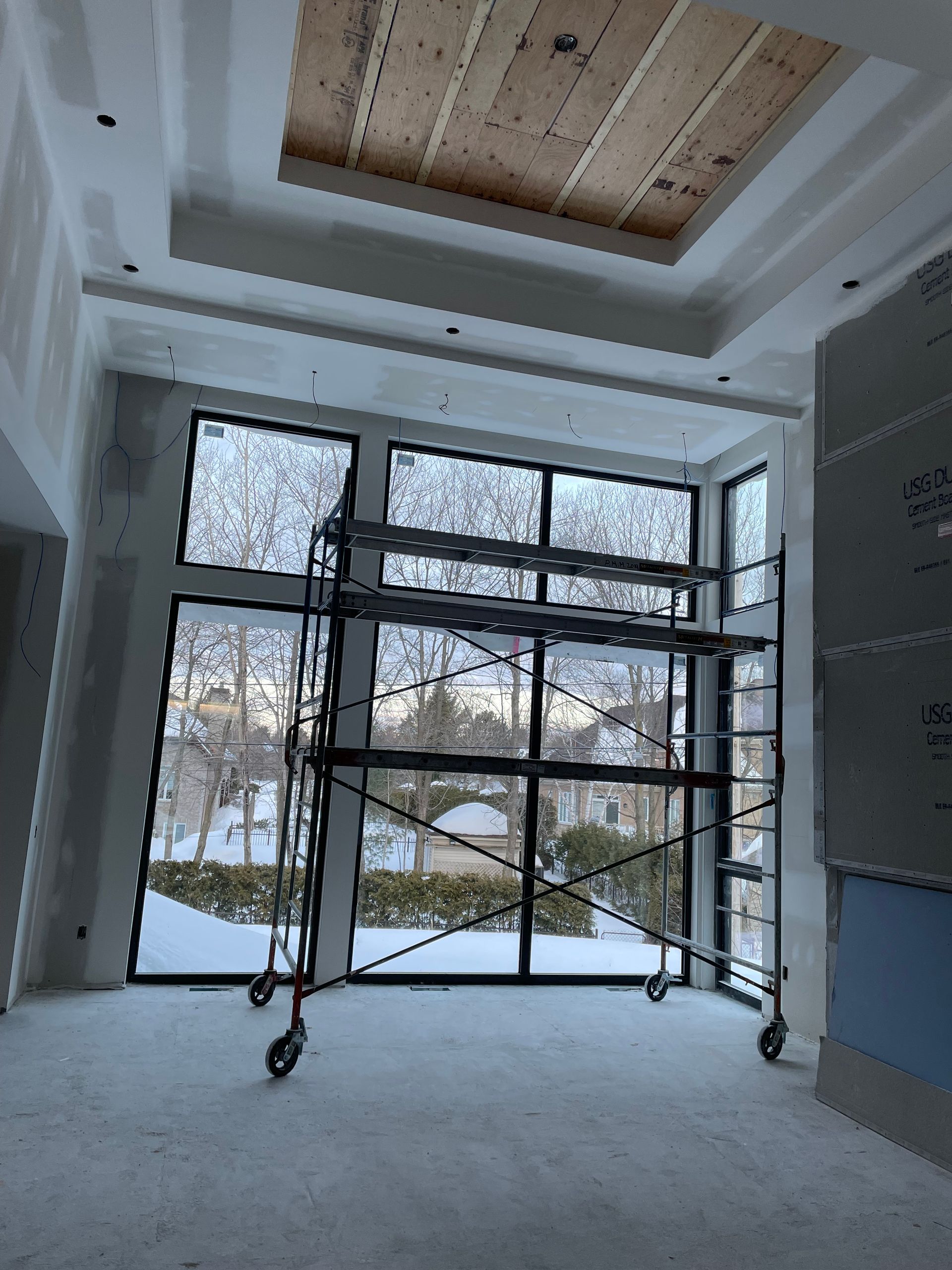 Vue intérieure d'une pièce en construction avec des échafaudages devant de grandes fenêtres.
